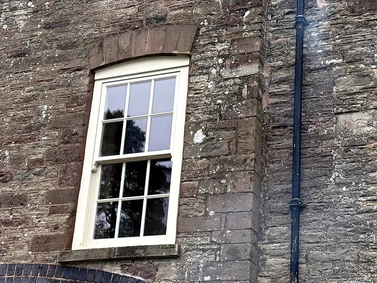 Cream timber sash window with a curved cambered head in red sandstone