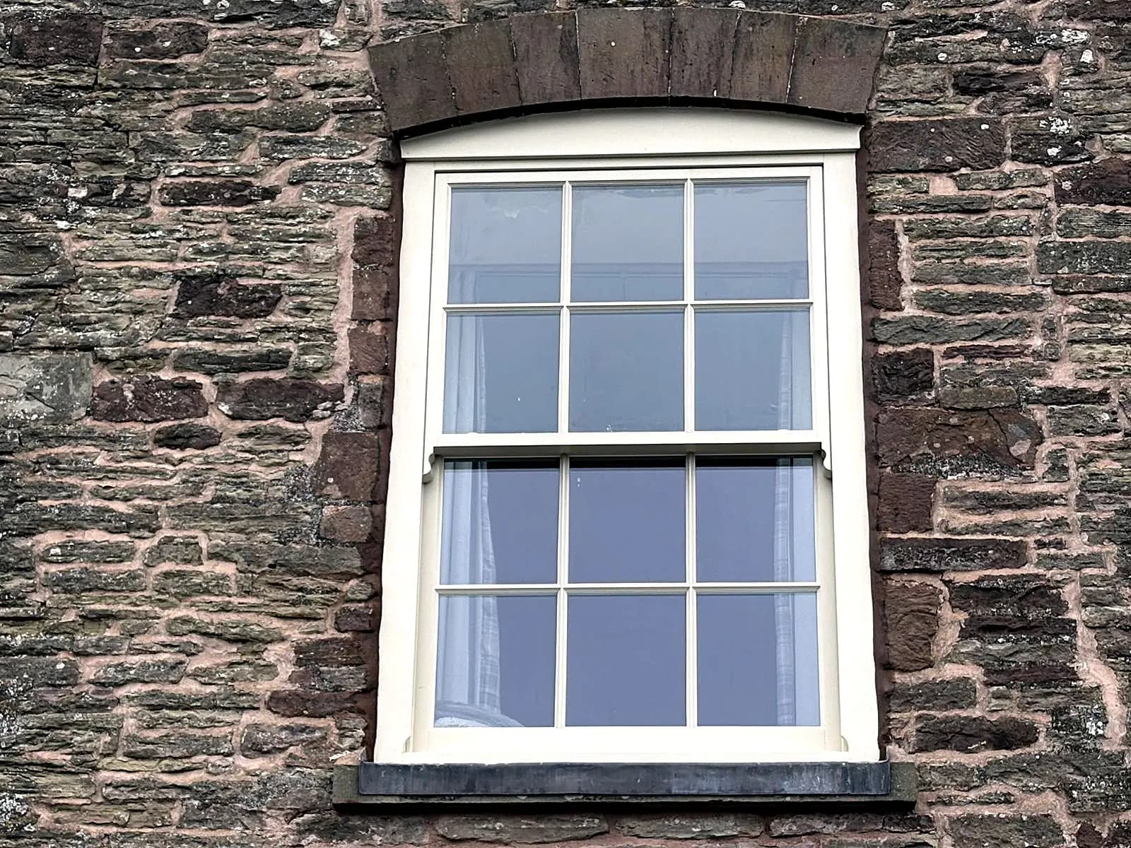 Cream six-over-six timber sash window set in a stone surround